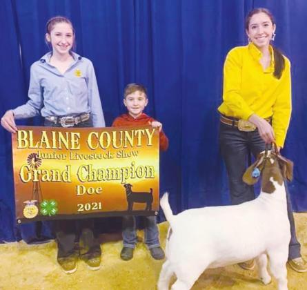 Reese Coleman (left) holds a sign for Riley Coleman (right) as she poses with her Grand Champion Doe (Photo provided by Watonga FFA)