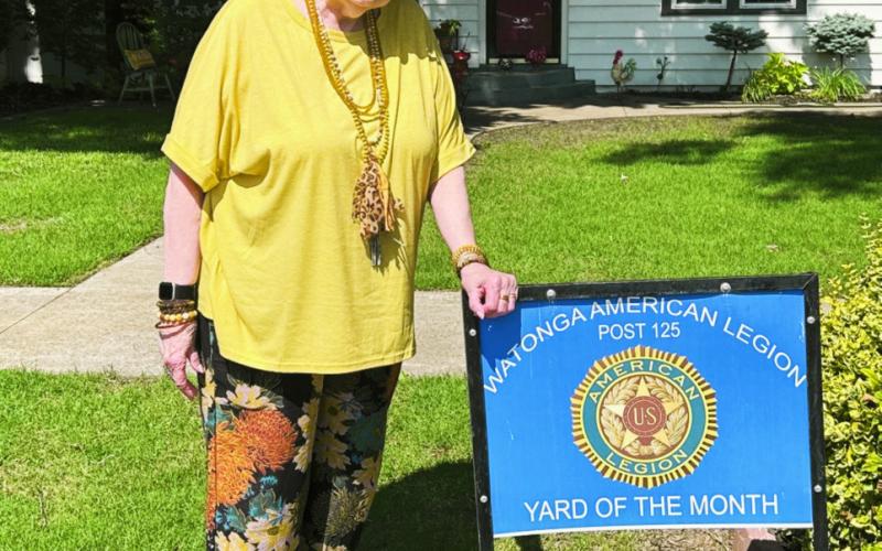Patt Curtin shows off her Yard of the Month sign presented for her neighborhood by the Watonga American Legion.