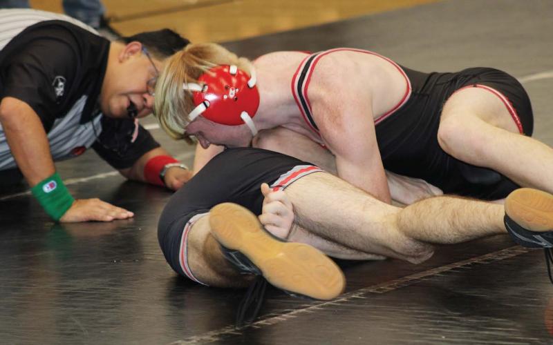 At top: A Bison athlete strong arms a Watonga wrestler. The ref is on the floor with the athletes to keep up with scoring. .Below, at right, Elliot Harrall takes hold of her opponent.