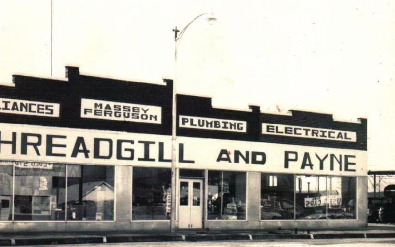 Members of the Watonga Foundation (above) removing siding applied to the front of LaWayne Flaming’s building in the 1960s or so, revealing the original paint underneath. A file photo (lower right) shows the building as it was before the craze to ‘modernize’ storefronts swept through town, covering up vintage graphics, windows and advertising.