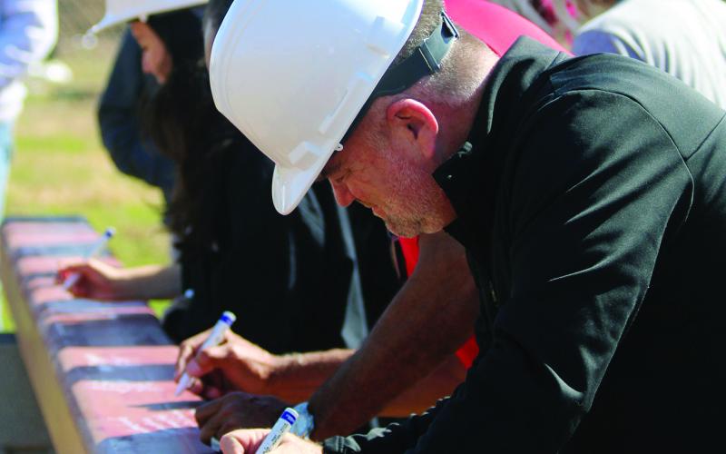 Watonga School Superintendent Kyle Hilterbran (foreground) signs the last beam in the new gym. The beam, with signatures, will be over the entrance, where it can be seen by all passersby.