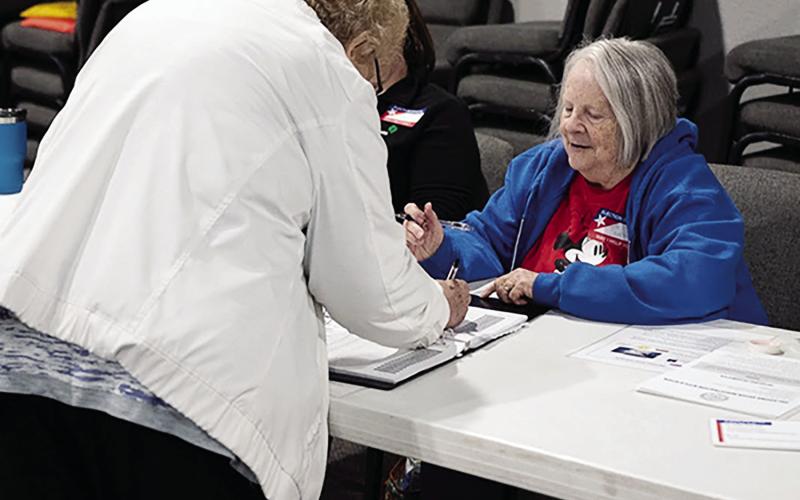 Poll worker Barbara Pennington holds a book of voter names while a Norman voter signs before receiving her ballot on March 7, 2023. Pennington has been volunteering as a poll worker for four years and said she has never worked the same location twice. (Whitney Bryen/Oklahoma Watch)