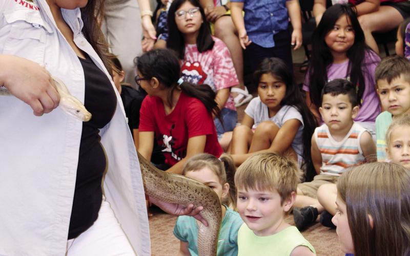 seated side by side. It was the kickoff of the summer reading program at the library, and if this was any indication, Watonga kids are going to spend the summer all together now, which is the theme of the program this year. Students at the Watonga Public Library hesitate slightly before touching Hazel, a granite python brought to the library Monday as part of Extreme Animals Event.