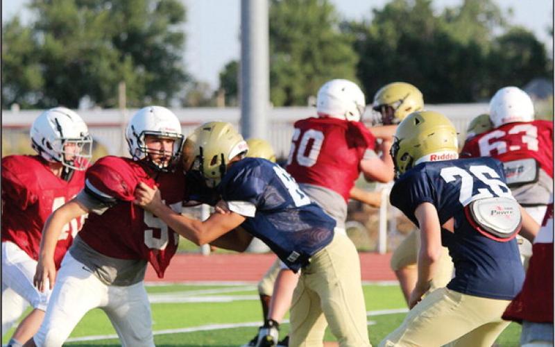 Above right: Starting quarterback Talen Smith rolls out of the pocket to launch a pass while a Fairview player scrambles in an attempt at a sack. At right: Landon Wagner takes a stop from a Kingfisher lineman all the while keeping his eyes on the play downfield