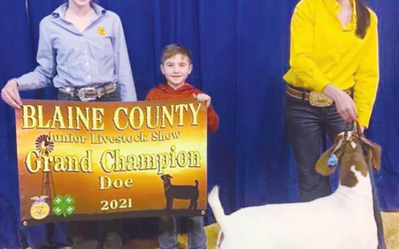 Reese Coleman (left) holds a sign for Riley Coleman (right) as she poses with her Grand Champion Doe (Photo provided by Watonga FFA)