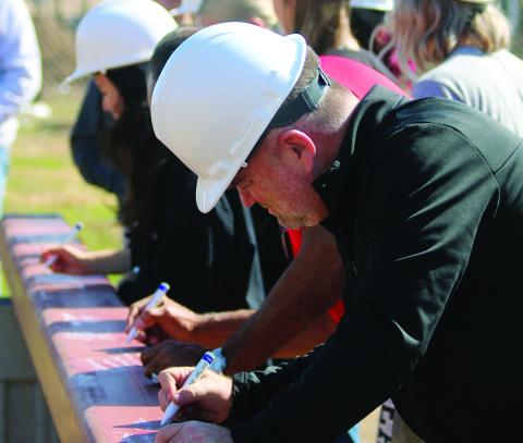 Watonga School Superintendent Kyle Hilterbran (foreground) signs the last beam in the new gym. The beam, with signatures, will be over the entrance, where it can be seen by all passersby.