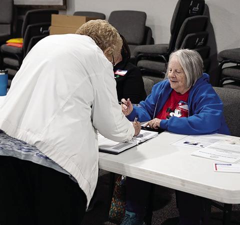 Poll worker Barbara Pennington holds a book of voter names while a Norman voter signs before receiving her ballot on March 7, 2023. Pennington has been volunteering as a poll worker for four years and said she has never worked the same location twice. (Whitney Bryen/Oklahoma Watch)