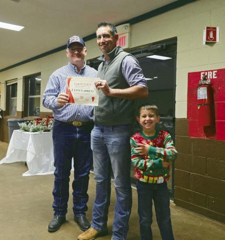 (L to R) Watonga Fire Chief Robert Daugherty presents Levi Garrett with a certificate naming him Watonga Volunteer Firefighter of the Year 2024. Garrett’s son, Jameson, is all grins over the event.